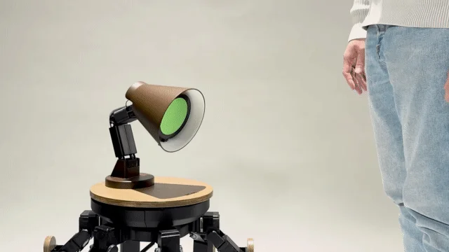 緑色の光を放つロボットのようなデバイスと、その前に立つ人物の脚