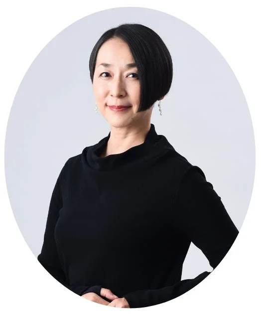 黒いトップスを着用したショートヘアのミドルエイジの女性が、優しい笑顔でカメラを見つめているポートレート写真